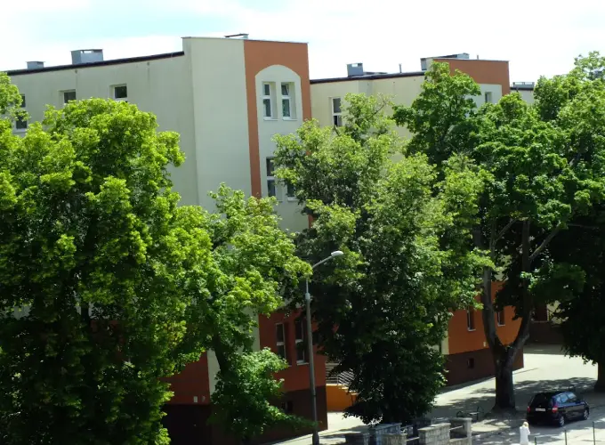 Budynek Wyższej Szkoły Informatyki i Zarządzania im. Prof. Tadeusza Kotarbińskiego w Olsztynie widoczny wśród drzew – naklejki na legitymacje studenckie i doktoranckie
