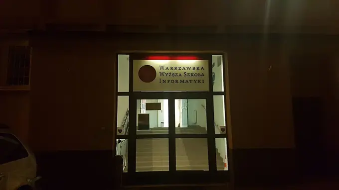 Oświetlone wejście do Warszawskiej Wyższej Szkoły Informatyki po zmroku